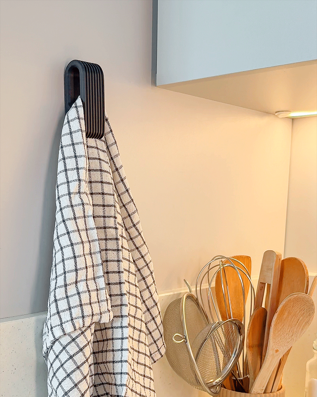 Dark ribbed towel clip mounted on wall holding a white grid-pattern dish towel in kitchen