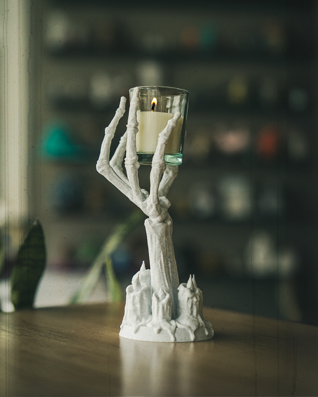 White skeleton hand candle holder with lit votive on wooden table